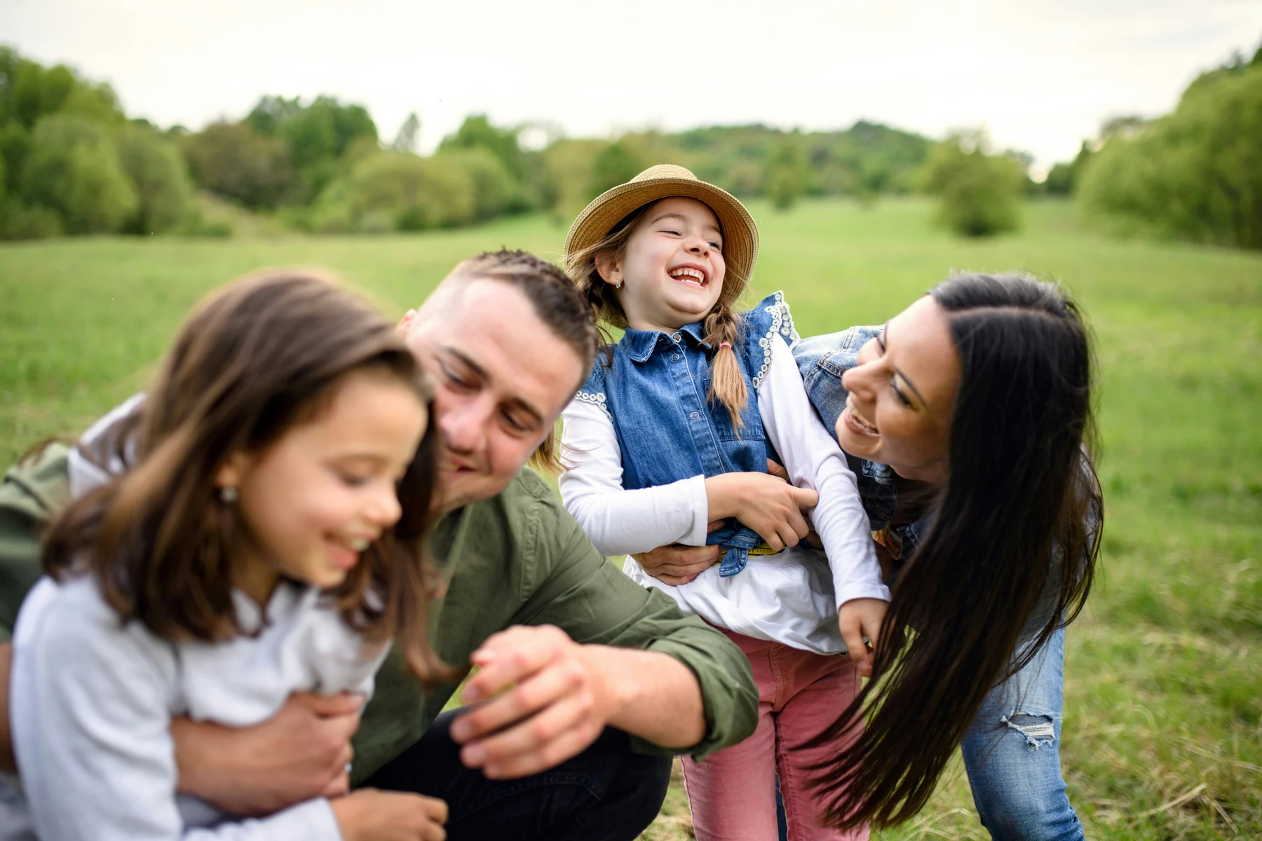 Parents and their two daughters laughing together outdoors.