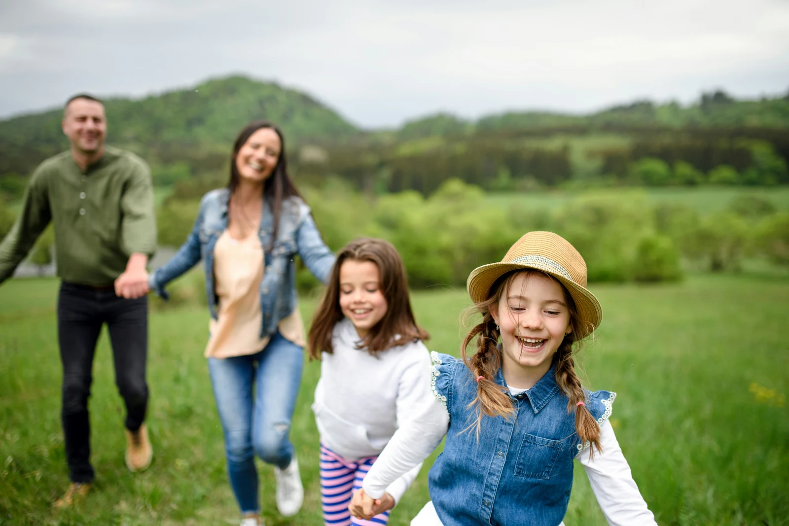 Two children leading their parents through a green meadow
