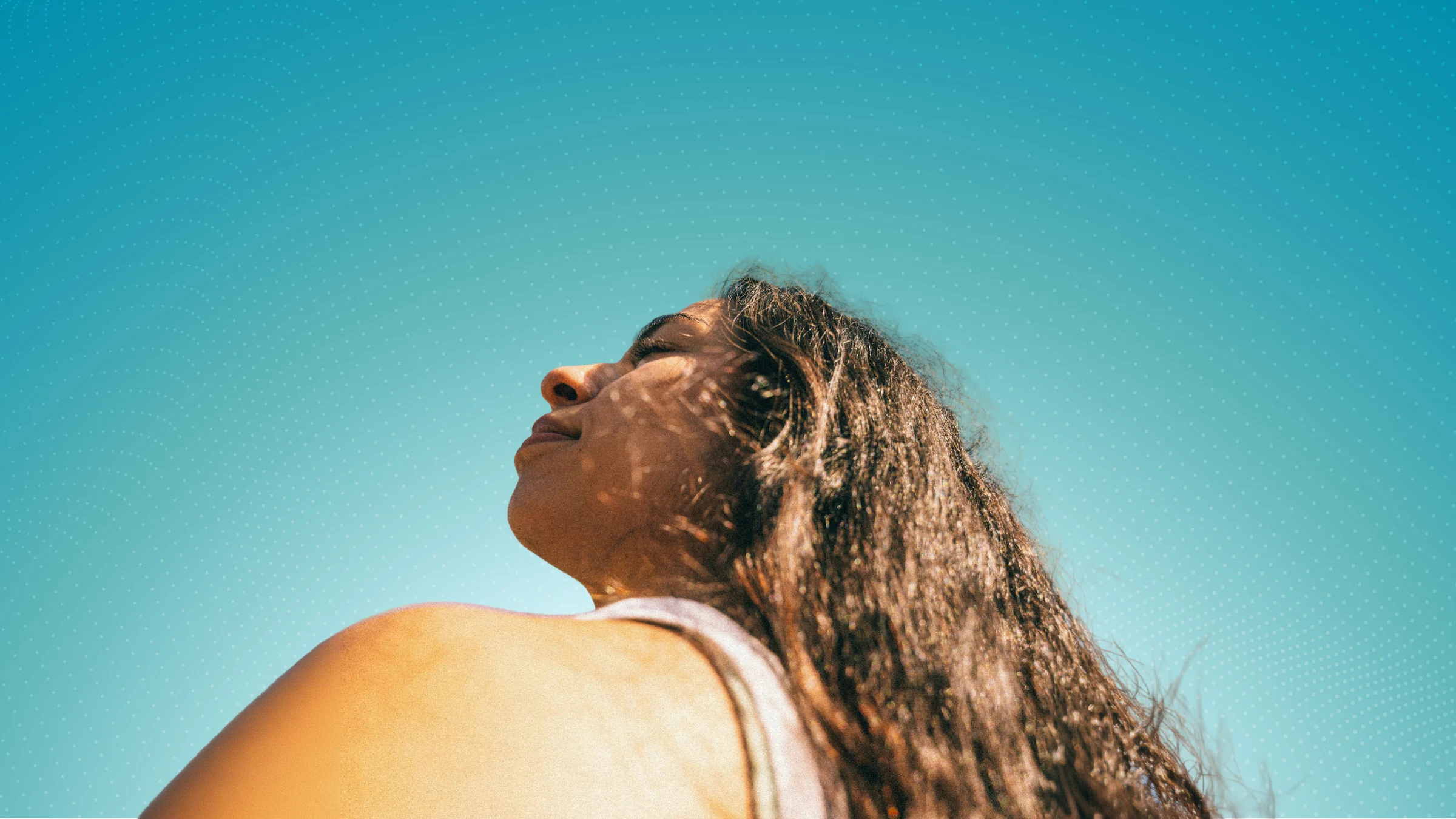 Woman enjoying the sunshine against Raxha’s teal patterned background.